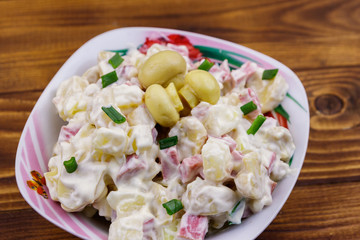 Potato salad with marinated mushrooms, sausage, onion and mayonnaise on wooden table