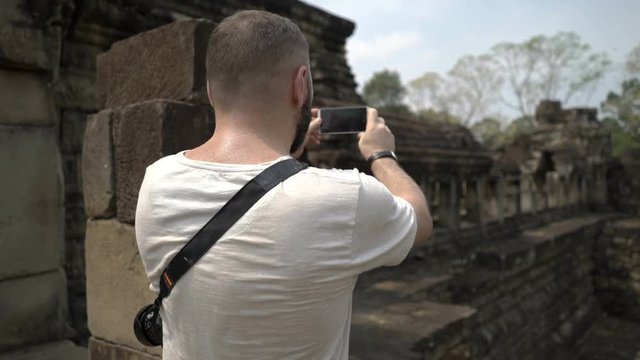 Tourist standing in old ruins and doing photos on smartphone