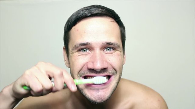 Young handsome guy brushing his teeth with a green toothbrush, smiling, looking into the camera.Portrait on white background.
