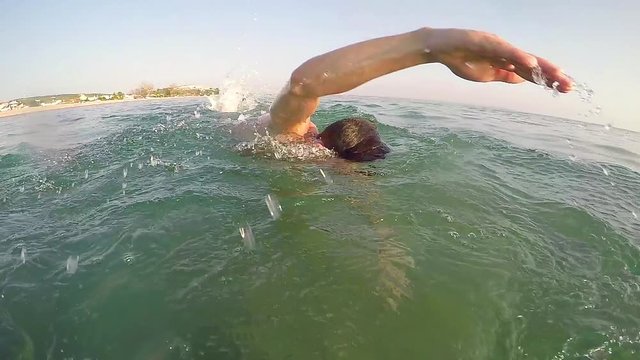 Young man swimming crawl in the lake, following shot of swimmer splashing toward camera, SLOW MOTION