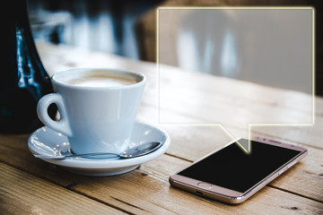 Mobile app text bubble next a cup of coffe on a wooden table. Frame blank space for advertising...