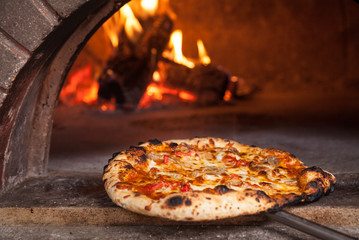 Pizza pie being taken out of a wood burning oven