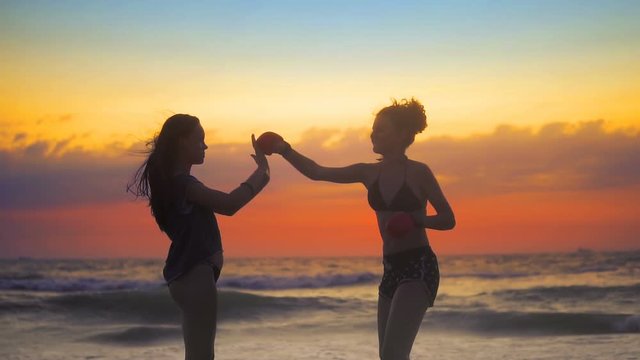 Two girls exercise, training karate on ocean beach against sunset sky and rolling waves, SLOW MOTION