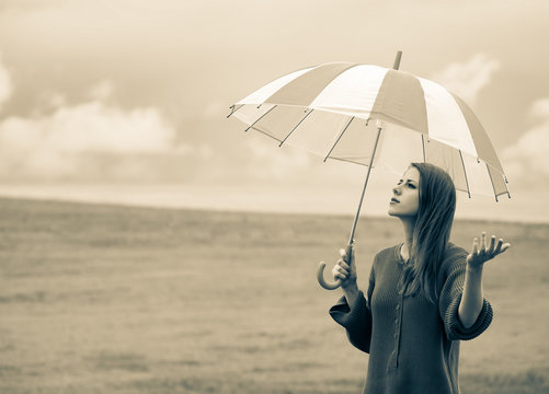 Beautiful adult girl in sweater with umbrella at wheat field and cloudscape on background. Image in sepia color style