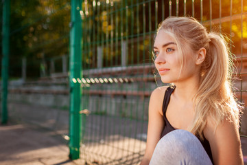 Young woman athlete having rest after running on sportsground in summer. Girl chilling outdoors in the morning