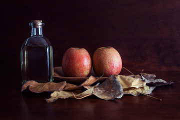 MANZANAS ROJAS SOBRE PLATO DE MADERA Y BOTELLA DE VINO DE CRISTAL Y HOJAS SECAS