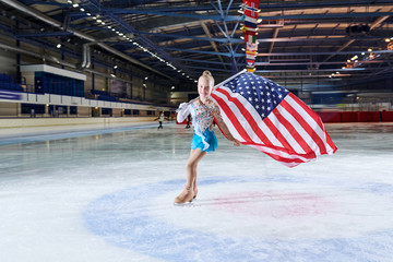 Full length portrait of smiling little girl figure skating carrying American flag in spotlight and...