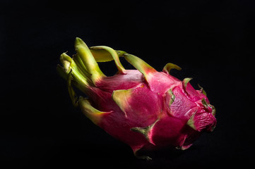 A whole, uncut dragon fruit isolated on black background.
