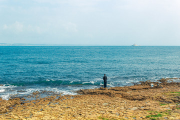 Fototapeta na wymiar Fisherman fishing in Oeiras with lighthouse on the horizon, Portugal