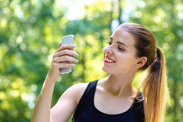 Young woman staring at her cellphone on a bright summer day in the forest