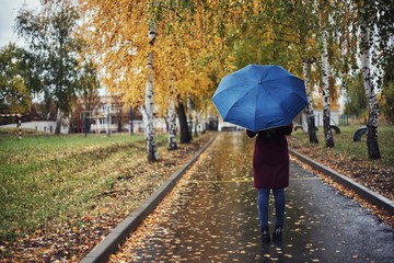 beautiful girl in a Burgundy coat with an umbrella on the background of yellow trees in cloudy weather.