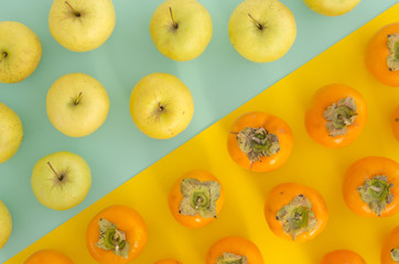 Fresh ripe persimmons and yellow apples bright split color background. Organic persimmon fruit and apple flat lay vibrant duotone background.