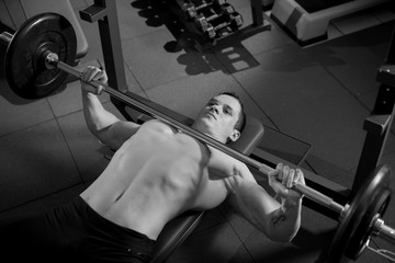 Brutal athletic man pumping up muscles on bench press