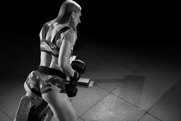 Fototapeta na wymiar Woman bodybuilder in gym lifting dumbbells on bench