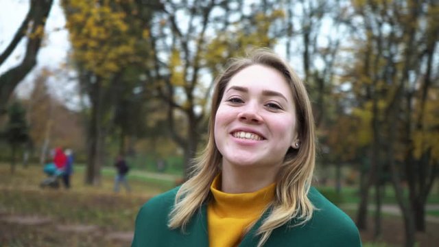 Autumn portrait of beautiful woman over yellow leaves while walking in the park in fall. The camera pans around the young woman. Girl is spinning. Blonde young girl in a green coat. 