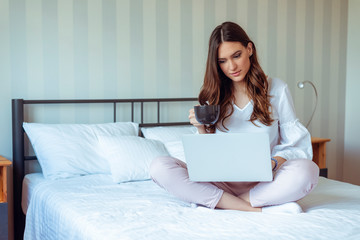 Attractive woman using laptop in morning and holding cup of coffee