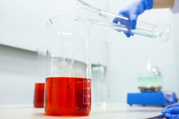 Hands of the scientist in the laboratory mixes with transfusion a chemical materials from graduated cylinder to beaker. Concept theme of applied chemistry - reaction, compound, solutions, dilution.