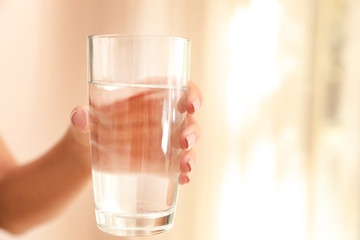 Woman holding glass with water on light background, closeup. Space for text