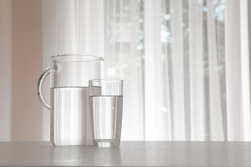 Jug and glass with water on table indoors. Space for text