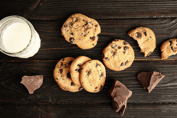 Flat lay composition with chocolate chip cookies and jar of milk on wooden background