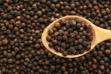 Spoon with black pepper over heap of grains, top view