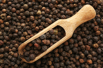 Scoop with black pepper on heap of grains, top view