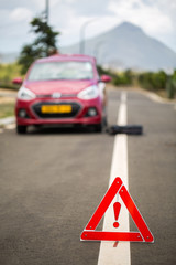 Broken car with a spare wheel and the sign on the background of mountains and palm trees.