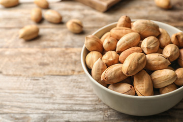 Pecan nuts in bowl on wooden table, space for text