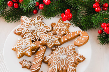 Christmas homemade gingerbread cookies and fir branches on white wooden background.