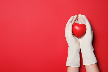Doctor in medical gloves holding heart on color background, top view. Space for text