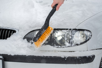 Woman cleaning snow from the car in the winter. Headlight of the car.
