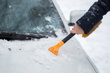 Woman cleaning snow from the car in the winter
