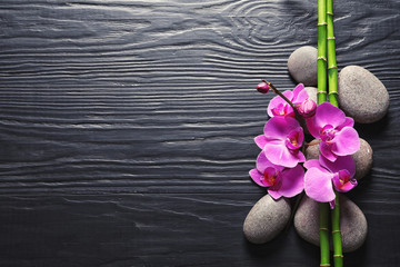 Spa stones with orchid flowers and bamboo on dark wooden background, top view. Space for text