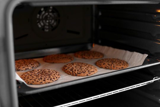 Open modern oven with freshly baked cookies on sheet, closeup