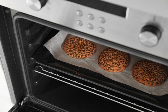 Open modern oven with freshly baked cookies on sheet, closeup