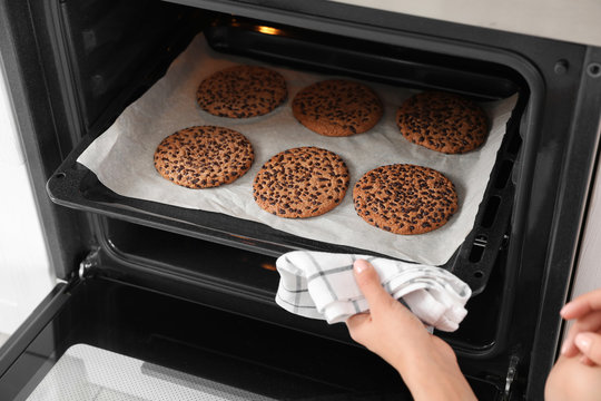 Young woman taking baking sheet with cookies from oven, closeup