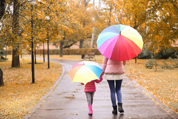 Mother and daughter with umbrellas taking walk in autumn park on rainy day