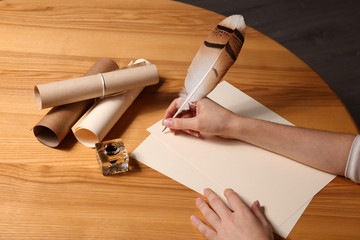 Woman using feather pen to write with ink on parchment at wooden table, closeup © New Africa