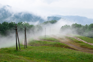 Mountain fog cover bright fresh meadow with electric pillars