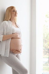 Portrait of beautiful pregnant woman near light wall