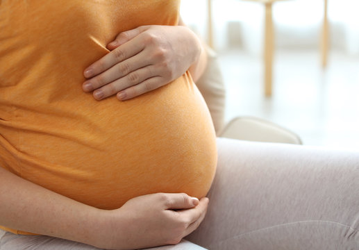 Pregnant woman sitting in light room at home, closeup