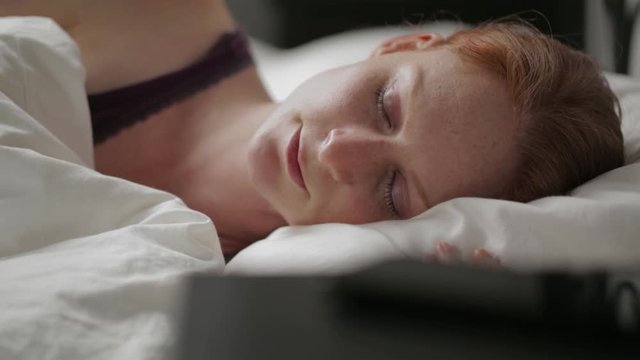 Static footage of a young woman sleeping in bed on her side.