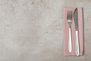 Fork, knife and linen napkin on grey background, top view. Space for text