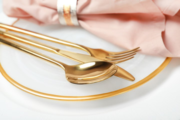 Plate with golden cutlery and napkin on table, closeup. Festive dinner setting