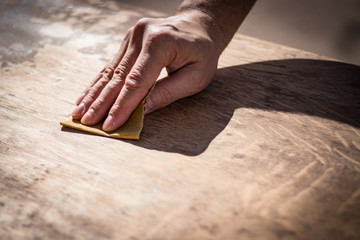 Gritty weathered man's hand and sandpaper; hand sanding a table top to refinish with paint or stain