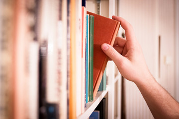 Hand pulling a classic book from a library bookshelf. - obrazy, fototapety, plakaty