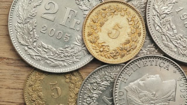 Closeup dolly footage of Swiss Franc coins over a wooden surface.