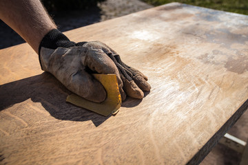 Hand in glove with sandpaper; sanding a table top to refinish with paint or stain