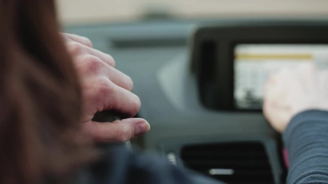 A female car driver enters and address in the satellite navigation of her car and holds the steering wheel.