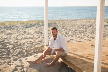 The man in the white shirt and shorts sitting on the beach.